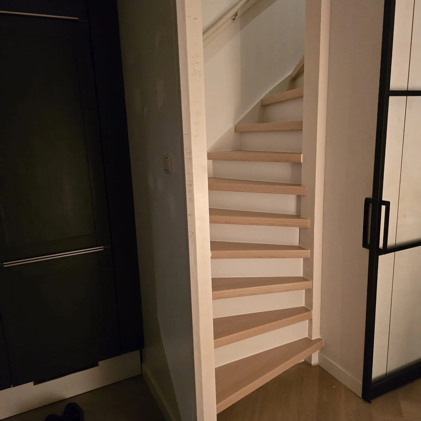 Trap met lichte houten treden naast een zwarte glazen deur
