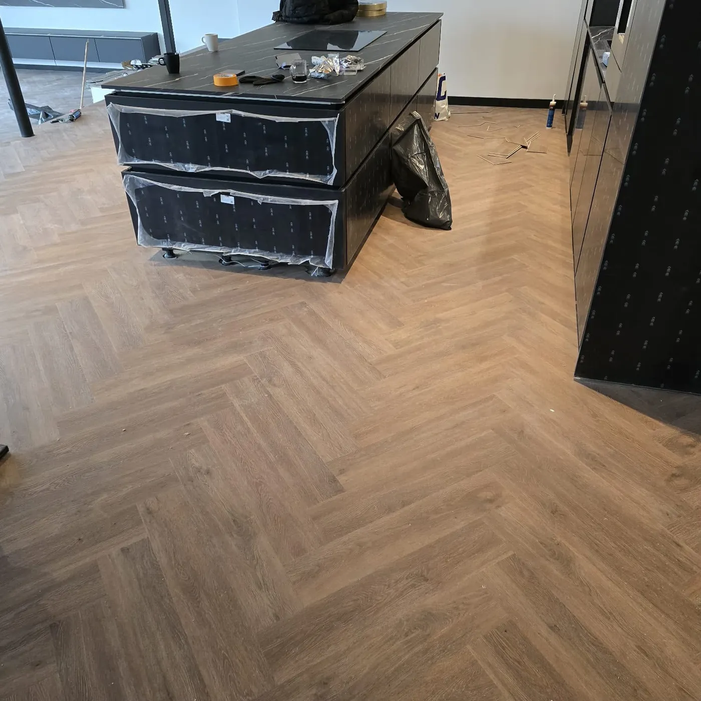 Visgraatvloer rond een zwart keukeneiland