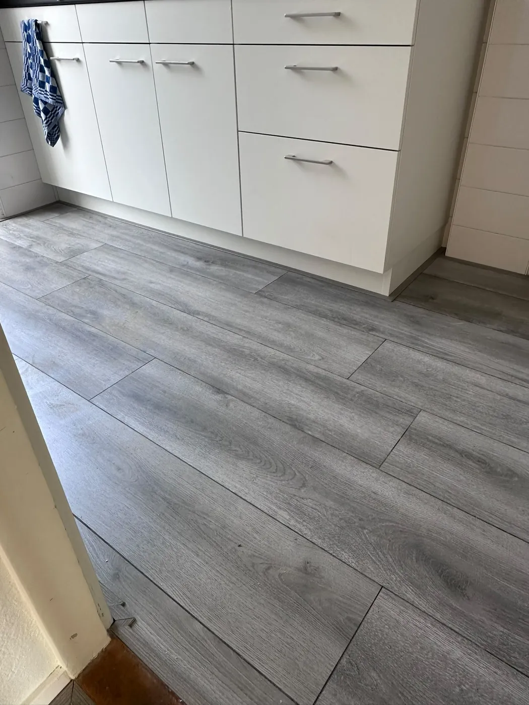 Grijze houtlook vloer naast een witte keukenkast