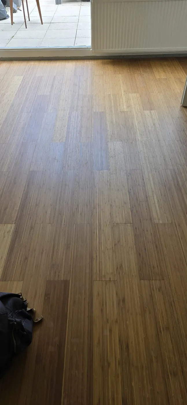 Donkere houten vloer met lange planken naast een raam